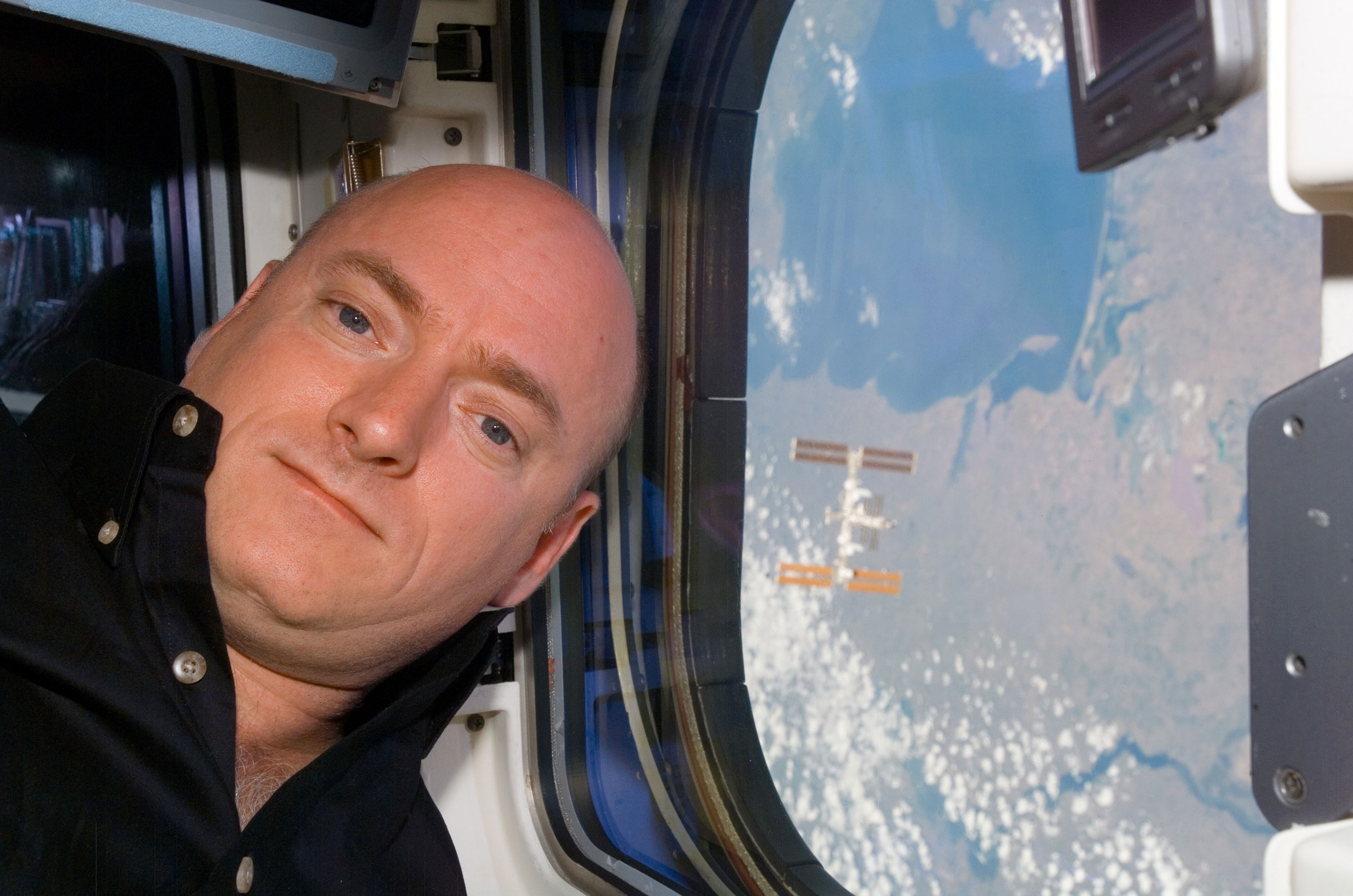 STS-118 Commander CDR Scott Kelly posing for a photo near a window on the Space Shuttle Endeavour. The International Space Station ISS is visible behind him. Credit: NASA