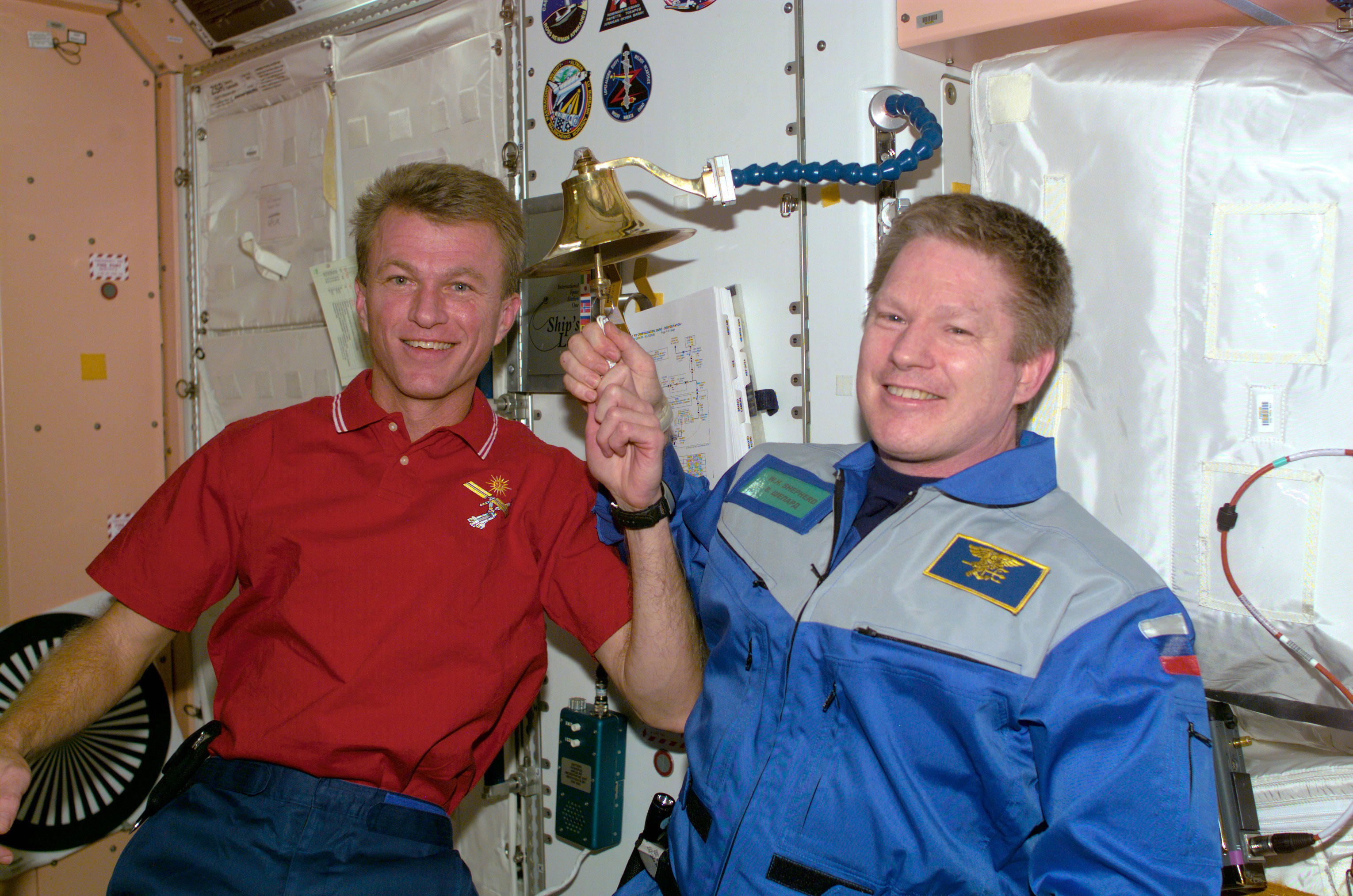 Astronauts Brent W. Jett, Jr. (left) and William M. Shepherd participate in an old Navy tradition of ringing a bell to announce the arrival or departure of someone to a ship.The bell is mounted on the wall in the Unity node of the International Space Station (ISS). Credit: NASA