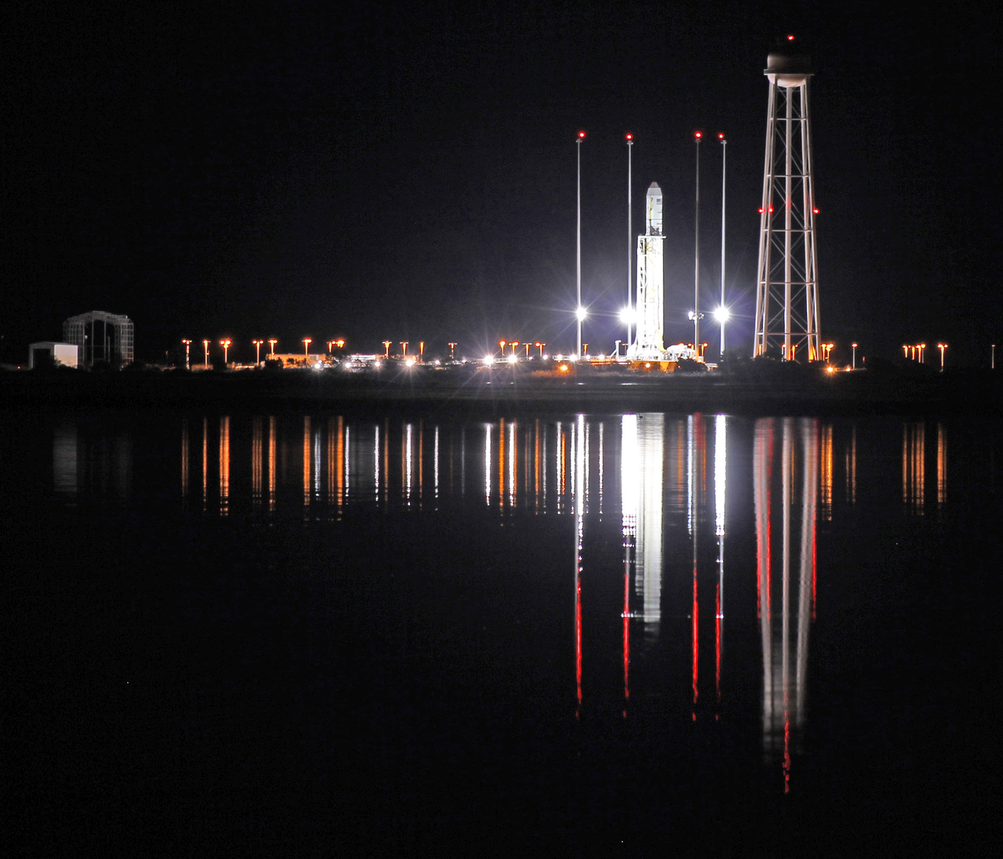 An Antares rocket stands erect, reflecting off the calm waters the night before its first night launch from NASA’s Wallops Flight Facility, VA. Credit: Ken Kremer