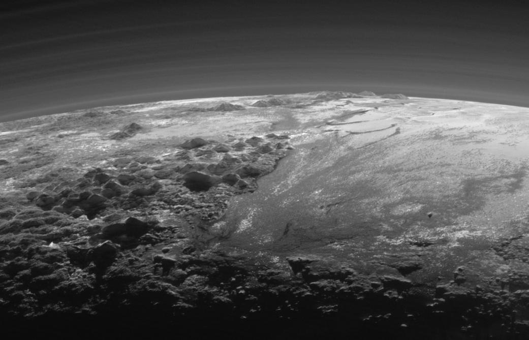 Figure 15: View looking back through Pluto’s atmosphere towards the Sun, shortly after New Horizons’ closest approach, showing the delicate structure and multiple haze layers of Pluto’s atmosphere. To the left foreground and on the horizon are, respectively, the icy mountains of Norgay Montes and Hillary Montes, named for the first conquerors of Mount Everest. The smooth expanse of Sputnik Planum is to the right. Credit: NASA/JHUAPL/SwRI